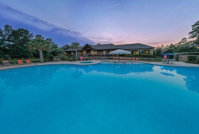 pool at dusk with a community pool and a patio