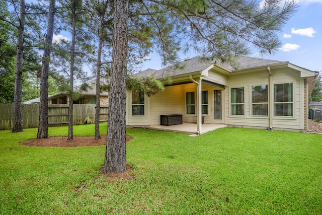 rear view of property featuring a yard, a shingled roof, fence, and a patio