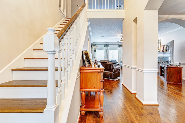 stairway with crown molding, a textured ceiling, hardwood / wood-style floors, and ceiling fan