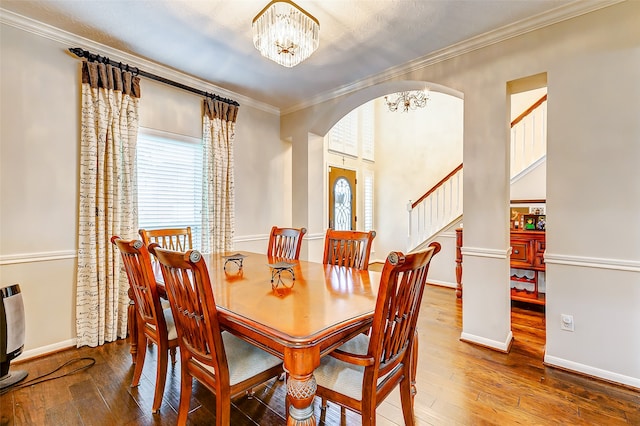 dining area with hardwood / wood-style floors, crown molding, a notable chandelier, and ornate columns