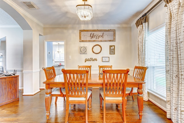 dining space with ornamental molding, a healthy amount of sunlight, wood-type flooring, and a notable chandelier