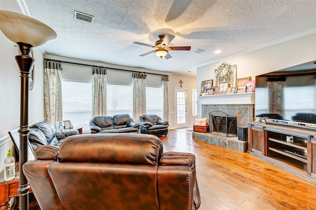 living room with a tiled fireplace, ornamental molding, a textured ceiling, ceiling fan, and hardwood / wood-style flooring