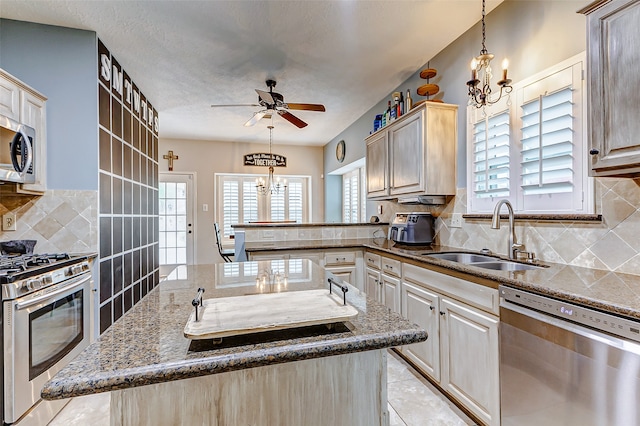 kitchen featuring ceiling fan with notable chandelier, backsplash, an island with sink, stainless steel appliances, and sink