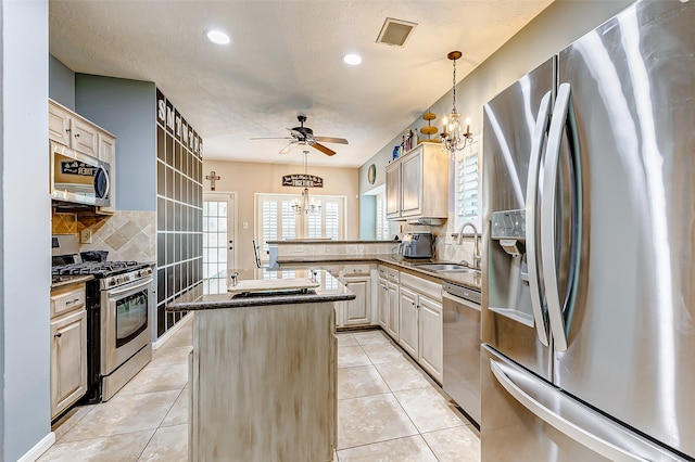 kitchen featuring ceiling fan with notable chandelier, appliances with stainless steel finishes, sink, a kitchen island, and decorative backsplash