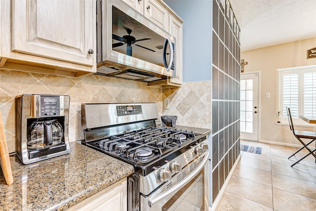 kitchen featuring backsplash, light stone countertops, stainless steel appliances, light tile patterned flooring, and ceiling fan