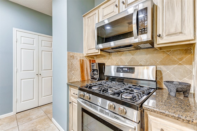 kitchen with light tile patterned floors, stainless steel appliances, light brown cabinets, decorative backsplash, and light stone counters