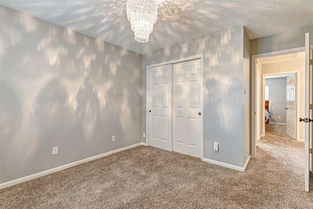 unfurnished bedroom with a textured ceiling, a closet, carpet floors, and a chandelier