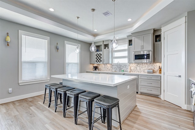 kitchen with a tray ceiling, a kitchen island, a wealth of natural light, and stainless steel microwave