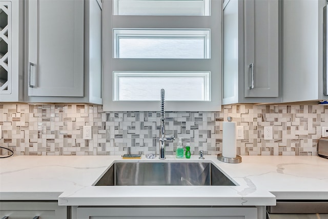 kitchen featuring sink, light stone countertops, gray cabinets, and tasteful backsplash