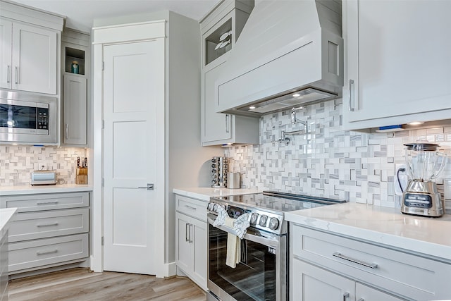 kitchen featuring light wood-type flooring, custom exhaust hood, tasteful backsplash, stainless steel appliances, and light stone countertops