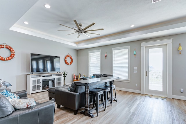 living room featuring ceiling fan, a fireplace, a raised ceiling, and light hardwood / wood-style flooring