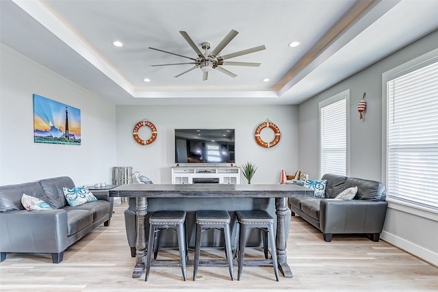 living room with ceiling fan, light wood-type flooring, and a tray ceiling