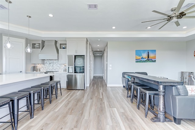 kitchen with premium range hood, ceiling fan, a breakfast bar, stainless steel fridge with ice dispenser, and light hardwood / wood-style floors