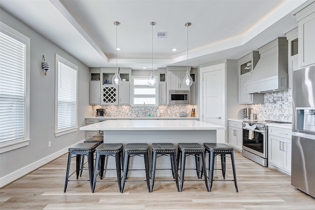 kitchen with a raised ceiling, a breakfast bar area, stainless steel appliances, decorative backsplash, and custom exhaust hood