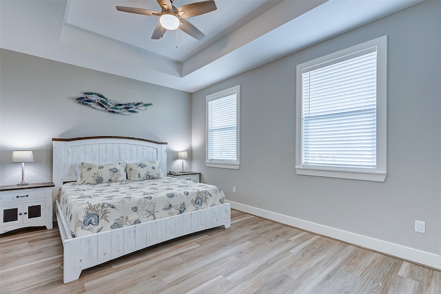 bedroom with light wood-type flooring, a raised ceiling, and ceiling fan