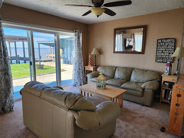 living room featuring a textured ceiling, a textured wall, light carpet, a water view, and a ceiling fan