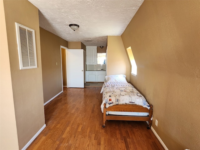 bedroom with a textured ceiling, connected bathroom, and wood-type flooring