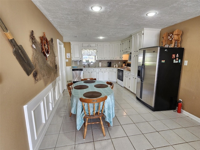 kitchen with light tile patterned floors, a textured ceiling, white cabinets, appliances with stainless steel finishes, and decorative backsplash