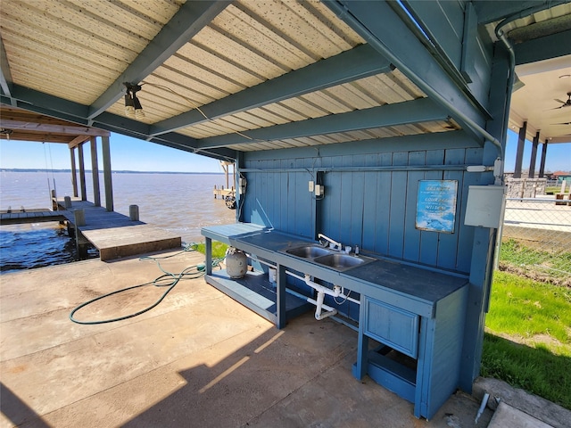 view of patio featuring a ceiling fan, a boat dock, a water view, fence, and a sink