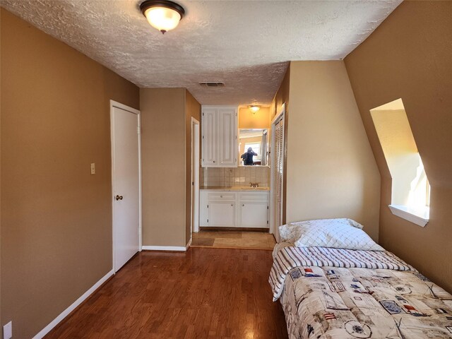 unfurnished bedroom featuring a textured ceiling, a closet, hardwood / wood-style floors, ensuite bath, and sink