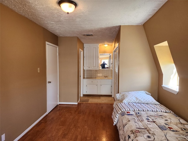 unfurnished bedroom with visible vents, a sink, a textured ceiling, wood finished floors, and baseboards