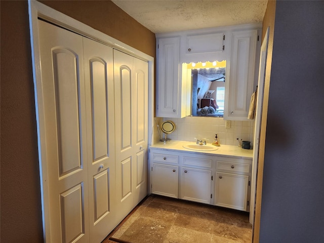 bathroom featuring tasteful backsplash, stone finish floor, a textured ceiling, and vanity