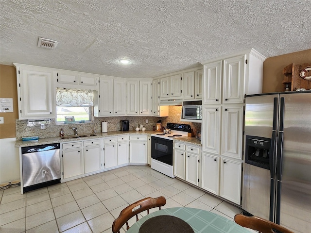 kitchen with stainless steel appliances, backsplash, white cabinets, a sink, and light tile patterned flooring