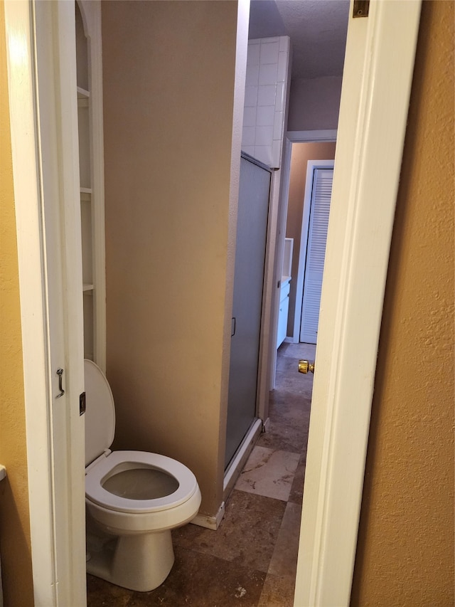 bathroom with a shower with door and toilet