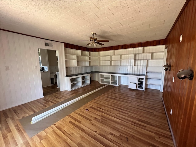 interior space with dark wood-type flooring, ceiling fan, and wood walls