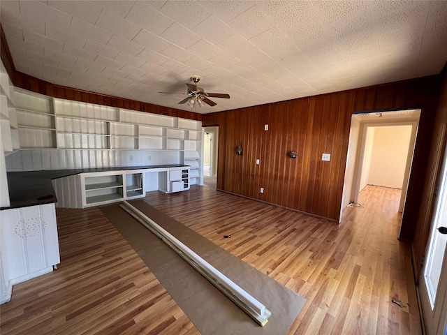 unfurnished living room featuring hardwood / wood-style flooring, ceiling fan, and wood walls