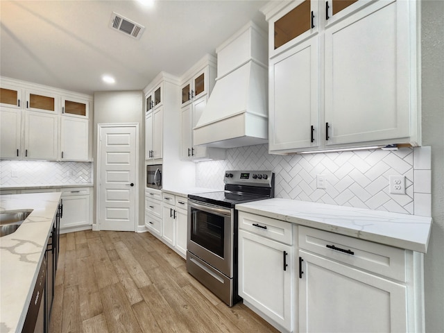 kitchen with white cabinets, backsplash, light hardwood / wood-style flooring, appliances with stainless steel finishes, and premium range hood