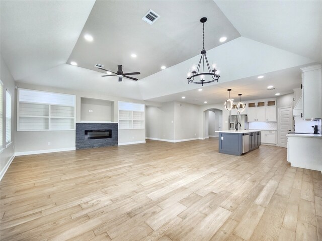 unfurnished living room featuring ceiling fan with notable chandelier, light wood-type flooring, vaulted ceiling, and a stone fireplace