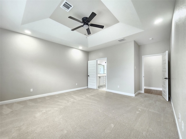 unfurnished bedroom with light carpet, a raised ceiling, connected bathroom, and ceiling fan