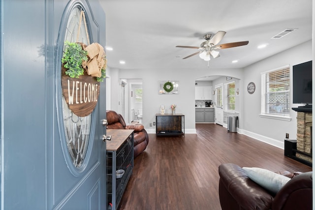 living room with dark hardwood / wood-style flooring, ceiling fan, and a stone fireplace