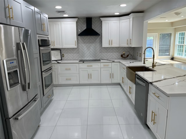 kitchen with white cabinetry, stainless steel appliances, light stone counters, sink, and wall chimney range hood