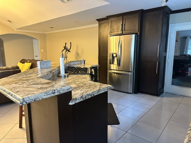 kitchen with an island with sink, light tile patterned flooring, light stone counters, and stainless steel refrigerator with ice dispenser