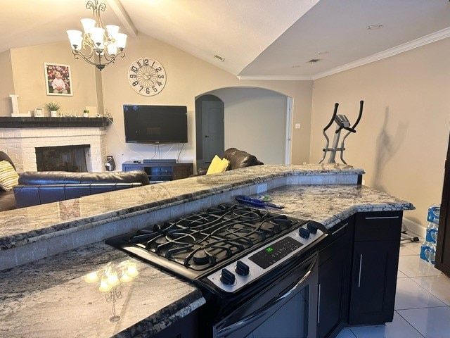 kitchen with light tile patterned floors, a fireplace, vaulted ceiling, gas range, and a chandelier