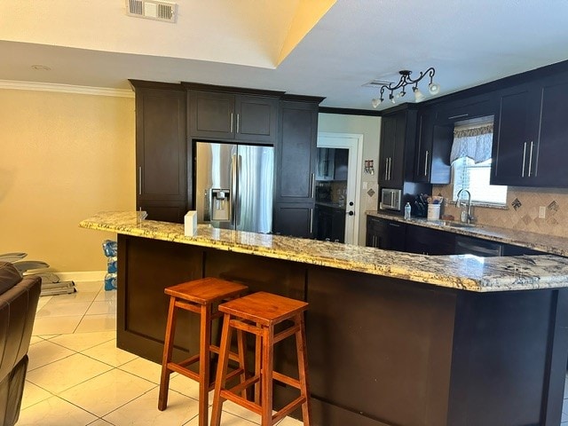 kitchen with light stone countertops, kitchen peninsula, stainless steel refrigerator with ice dispenser, a kitchen breakfast bar, and decorative backsplash