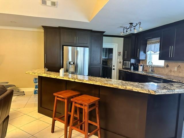 7410 Ashmole Ln, Houston, TX 77088 - kitchen featuring stainless steel fridge with ice dispenser, ornamental molding, light stone countertops, light tile patterned floors, and a breakfast bar