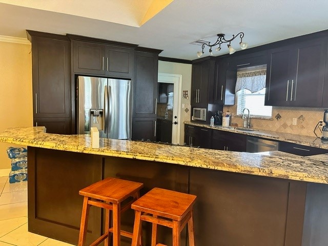 kitchen featuring light stone counters, stainless steel appliances, kitchen peninsula, and a breakfast bar