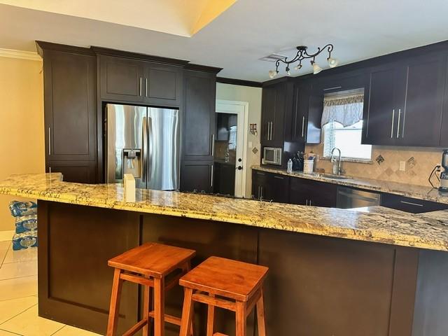 7410 Ashmole Ln, Houston, TX 77088 - kitchen featuring appliances with stainless steel finishes, light stone countertops, crown molding, light tile patterned floors, and a breakfast bar area