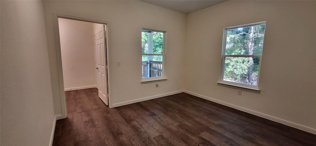 empty room featuring baseboards, a healthy amount of sunlight, and dark wood-style flooring