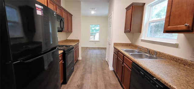 kitchen with a sink, brown cabinets, black appliances, and wood finished floors