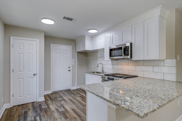 kitchen featuring appliances with stainless steel finishes, kitchen peninsula, white cabinetry, and dark hardwood / wood-style flooring