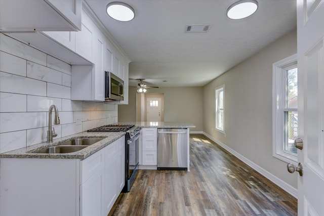 kitchen with sink, kitchen peninsula, white cabinetry, appliances with stainless steel finishes, and dark hardwood / wood-style floors