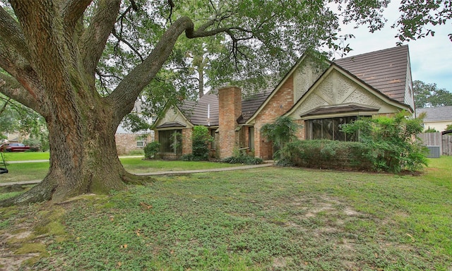 english style home featuring a chimney, a front lawn, and brick siding