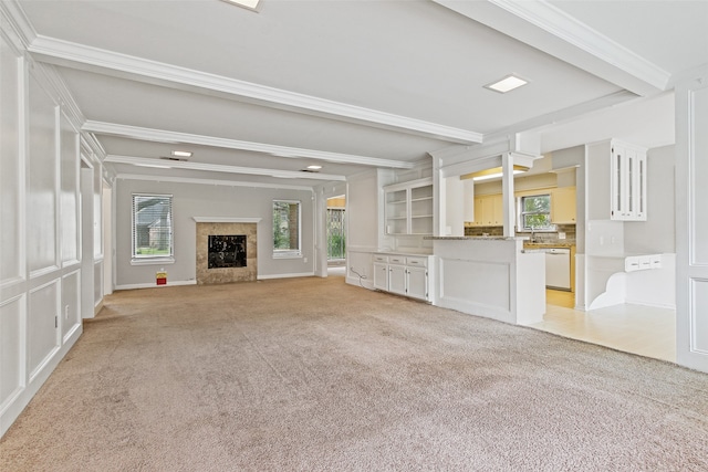 unfurnished living room with light colored carpet, a fireplace, beam ceiling, and crown molding