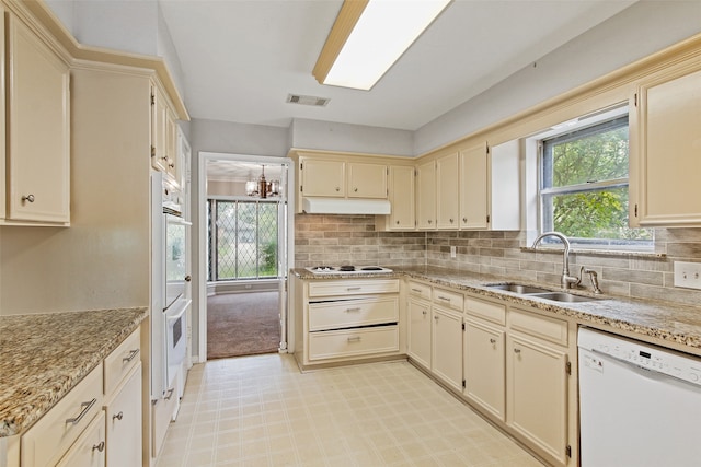 kitchen with white appliances, light stone countertops, sink, cream cabinetry, and tasteful backsplash