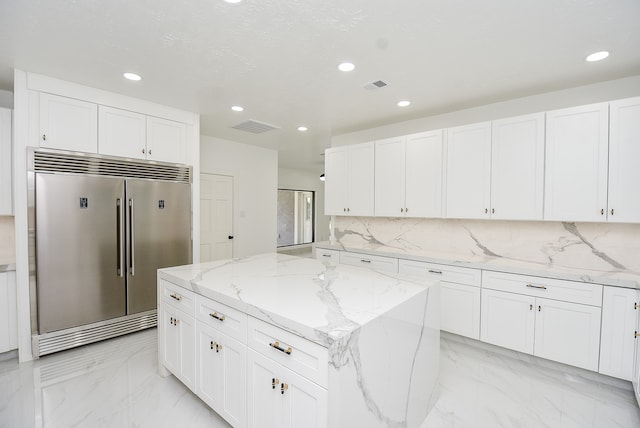 kitchen featuring a center island, light stone counters, stainless steel built in refrigerator, and white cabinets