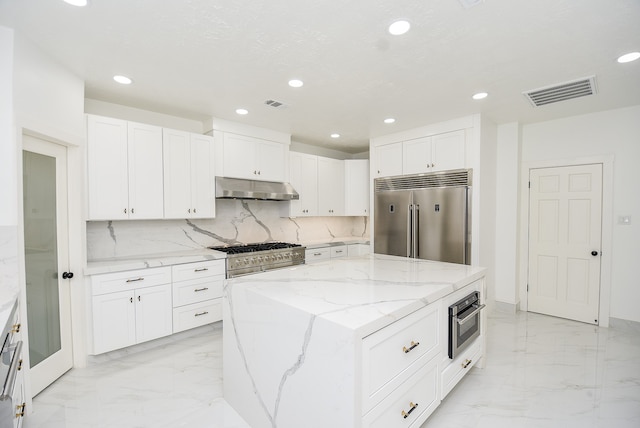 kitchen featuring high end appliances, light stone counters, a center island, decorative backsplash, and white cabinets